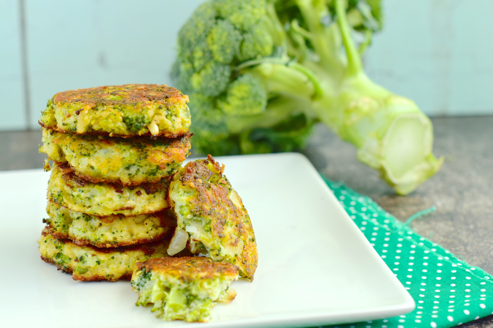 a stack of 5 baked broccoli fritters in front of a large crown of broccoli