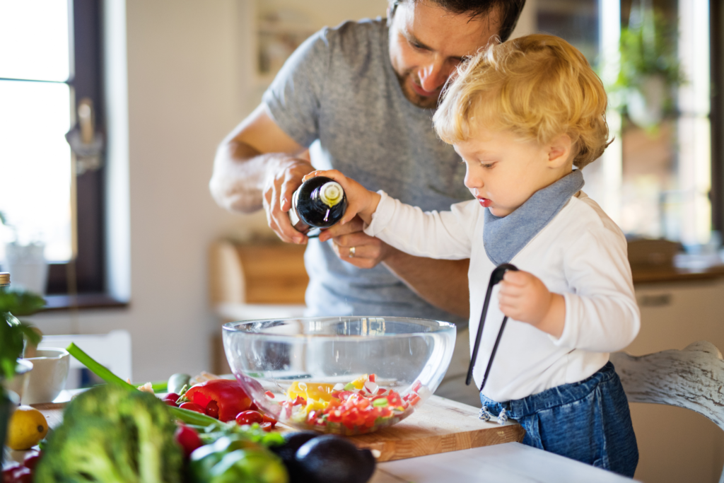 a blonde boy toddler cooking and his day preparing a salad for dinner