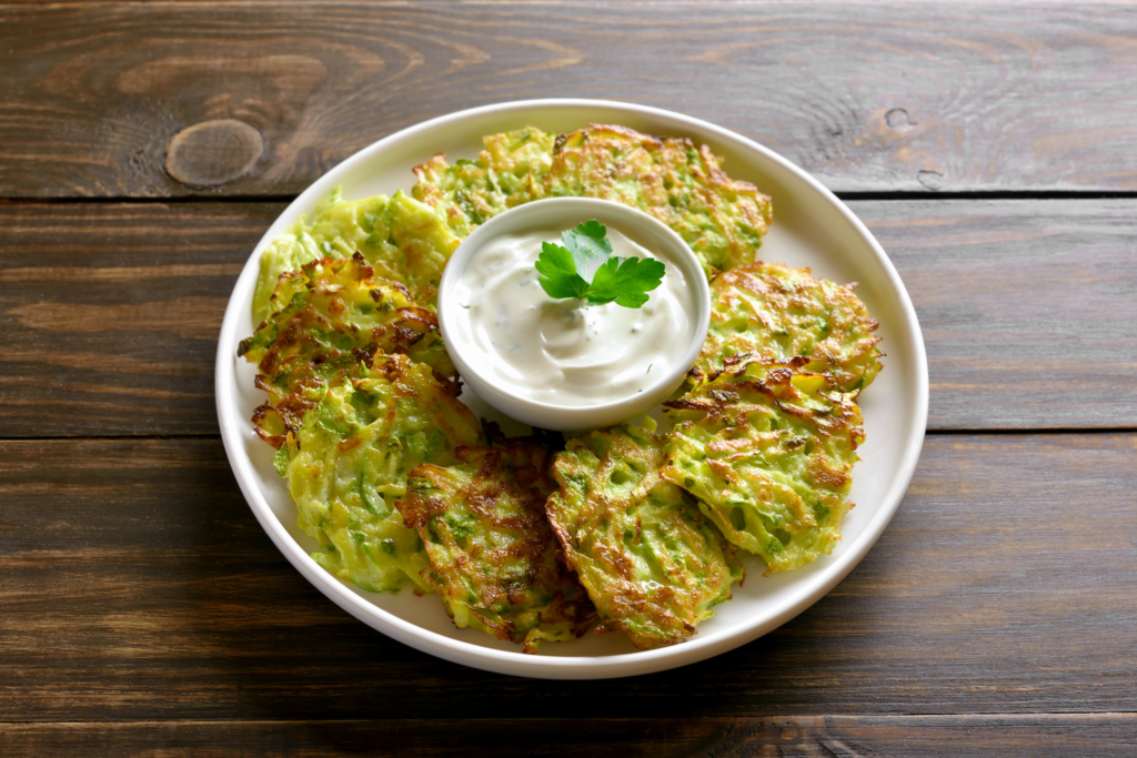 a dish of 9 zucchini fritters circled around a sour cream dip