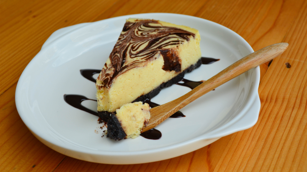 a slice of Chocolate Marble Cheesecake on a round, white plate with chocolate drizzle